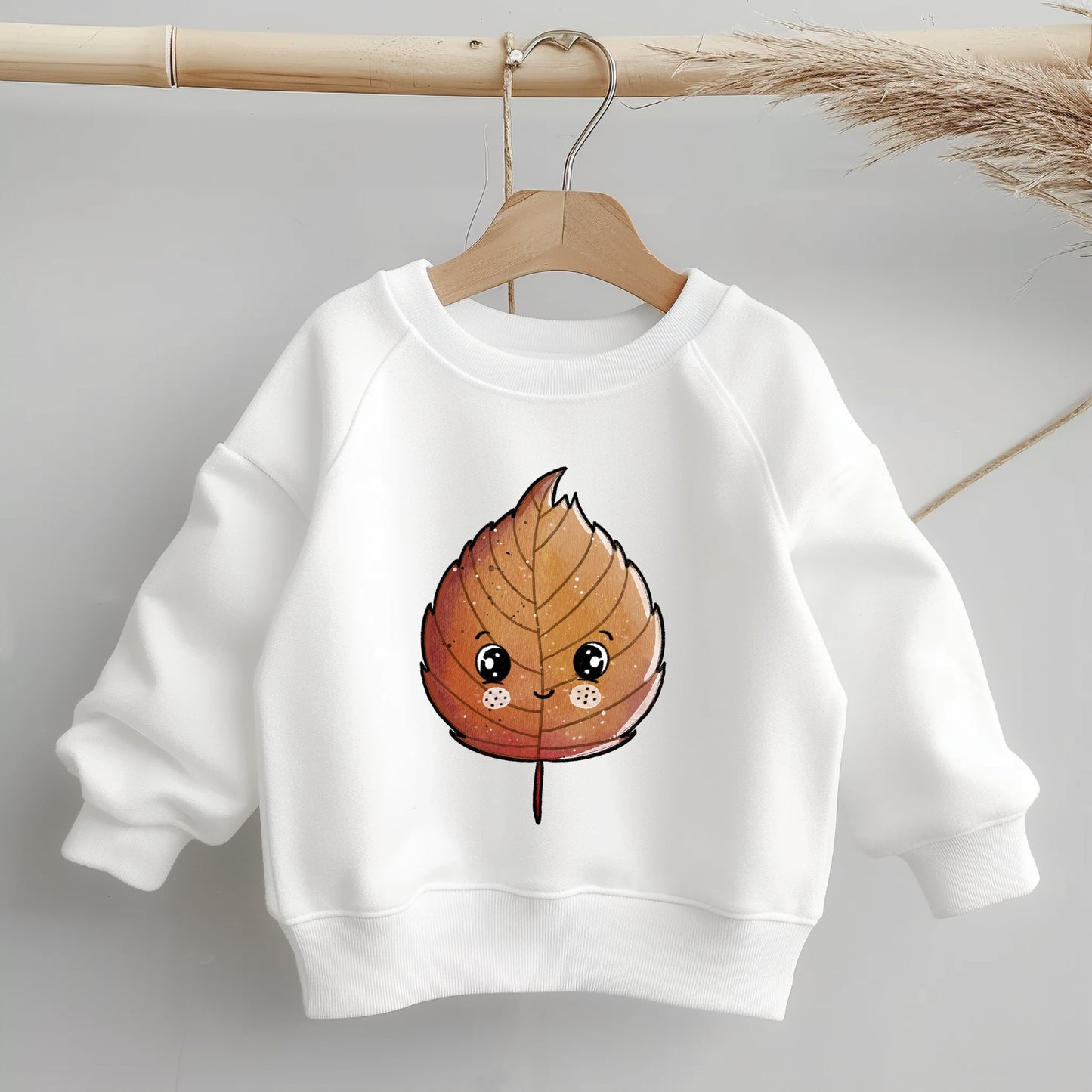 „Kinder-Sweater mit mittig platziertem braunen Buchenblatt-Bügelbild; zeigt Größe und Position des Motivs deutlich auf dem Kleidungsstück.“