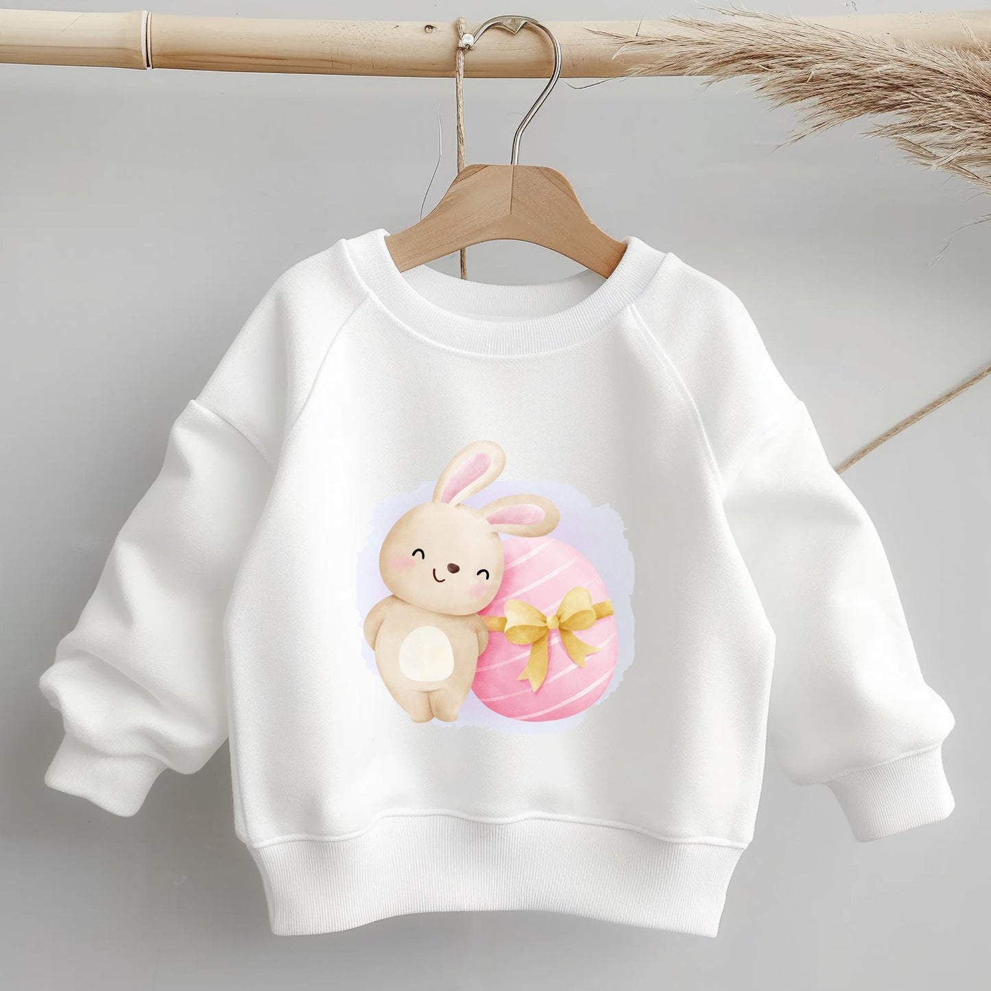 Bügelbild "Hase mit Schleifenosterei" auf weißem Kinderpullover – Oster-Motiv für DIY-Projekte.
