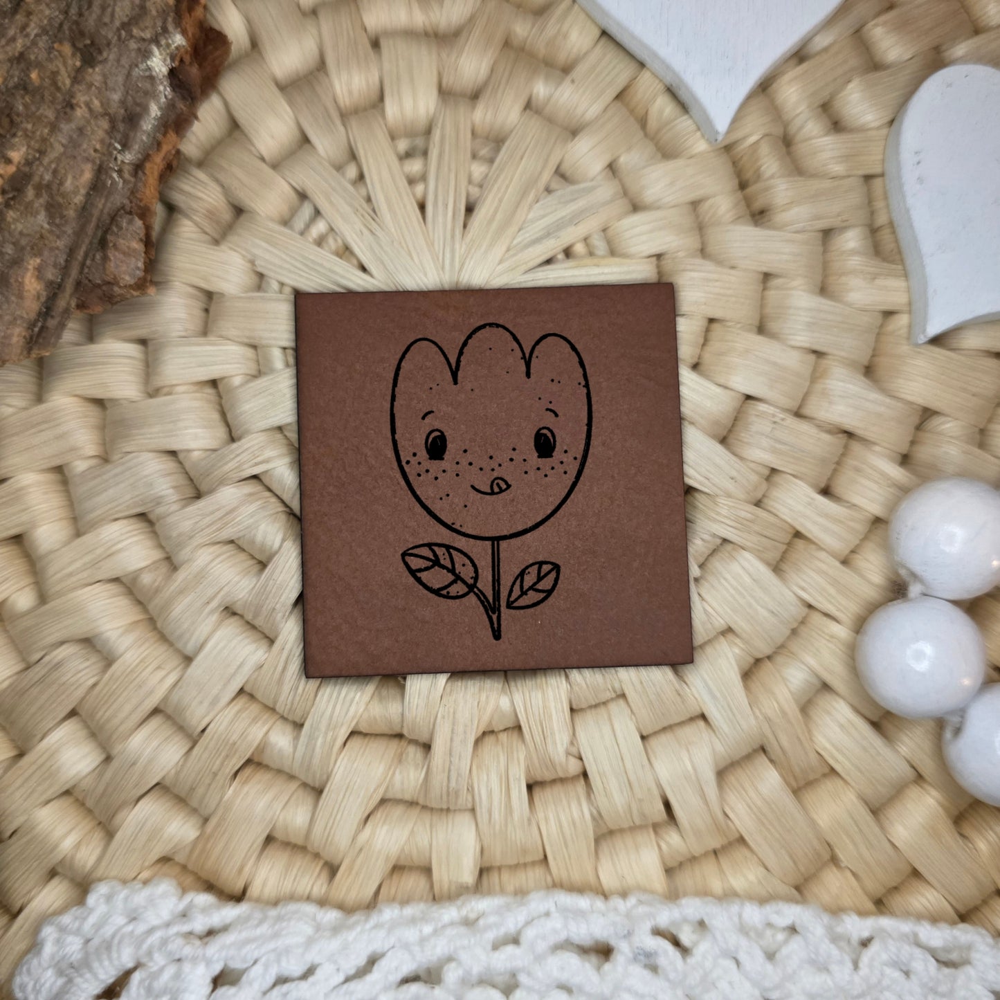 Kunstlederlabel „Buntes Glück“ mit fröhlicher Blumenillustration ohne Brille, schwarz graviert auf braunem Kunstleder, 4×4 cm