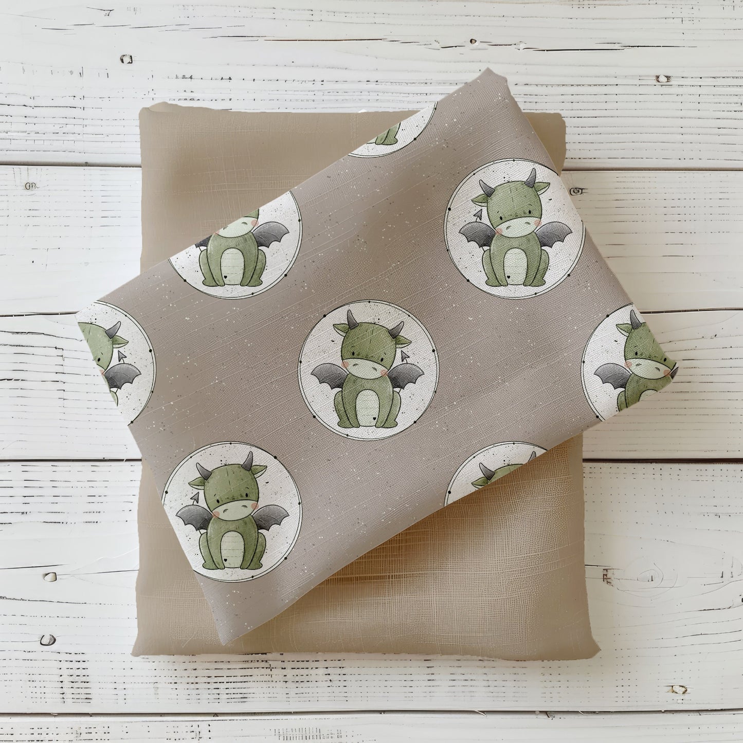 Mockup: Stoff „Button Drache“ mit wiederholten runden Drachen-Buttons auf taupefarbenem Hintergrund; sanfte Salbei- und Grautöne, feine Sprenkel; der Druck liegt diagonal auf passendem Uni-Kombistoff.