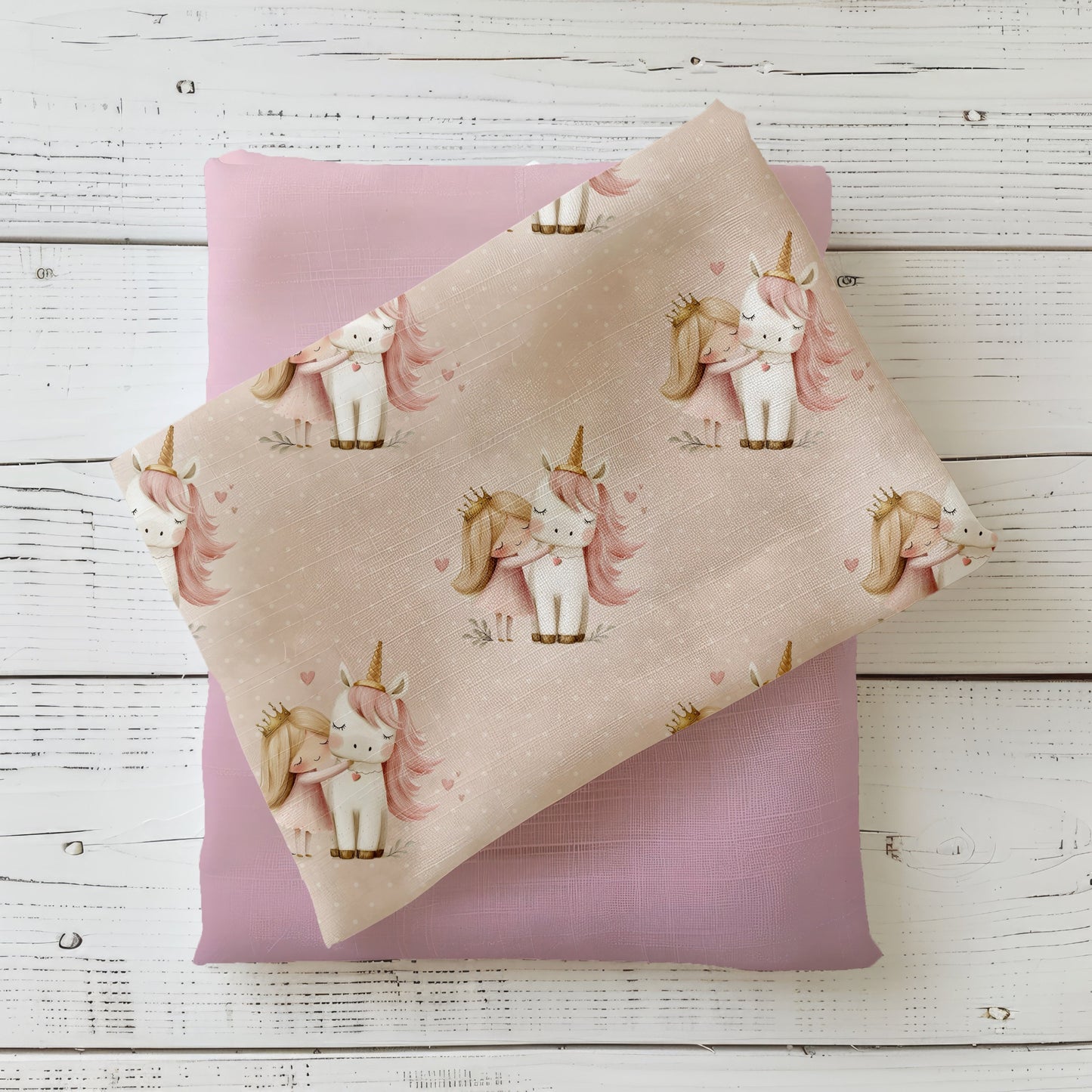 Mockup: Stoff „Einhorn & Prinzessin“ – weißes Einhorn mit rosa Mähne und Prinzessin mit Krone, kleine Herzen auf rosé-beigem Grund; Stoffkachel diagonal auf passendem Uni in Nude/Rosé als Kombi.