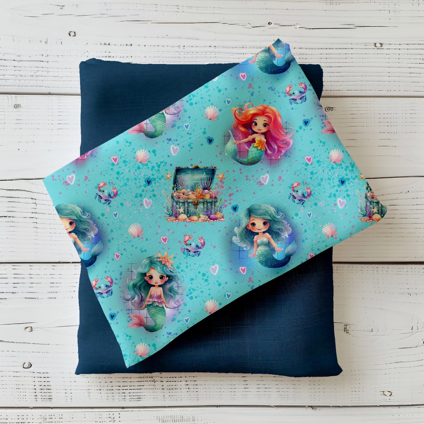 Mockup: Stoff „Kleine Meerjungfrau“ – niedliche Meerjungfrauen in Türkis & Koralle mit Herzen, Muscheln, Krebsen und Schatztruhe auf aquablauem Hintergrund; Stoffkachel diagonal auf passendem Uni als Kombi.