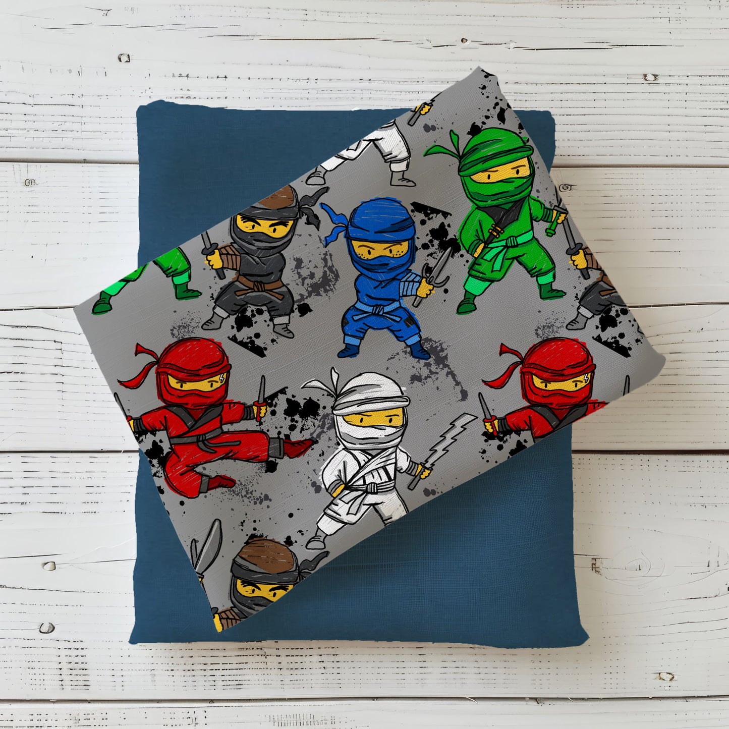 Gefalteter grauer Stoff mit fröhlich bunten Ninjas – modisches und verspieltes Outfit für kleine Action-Fans.