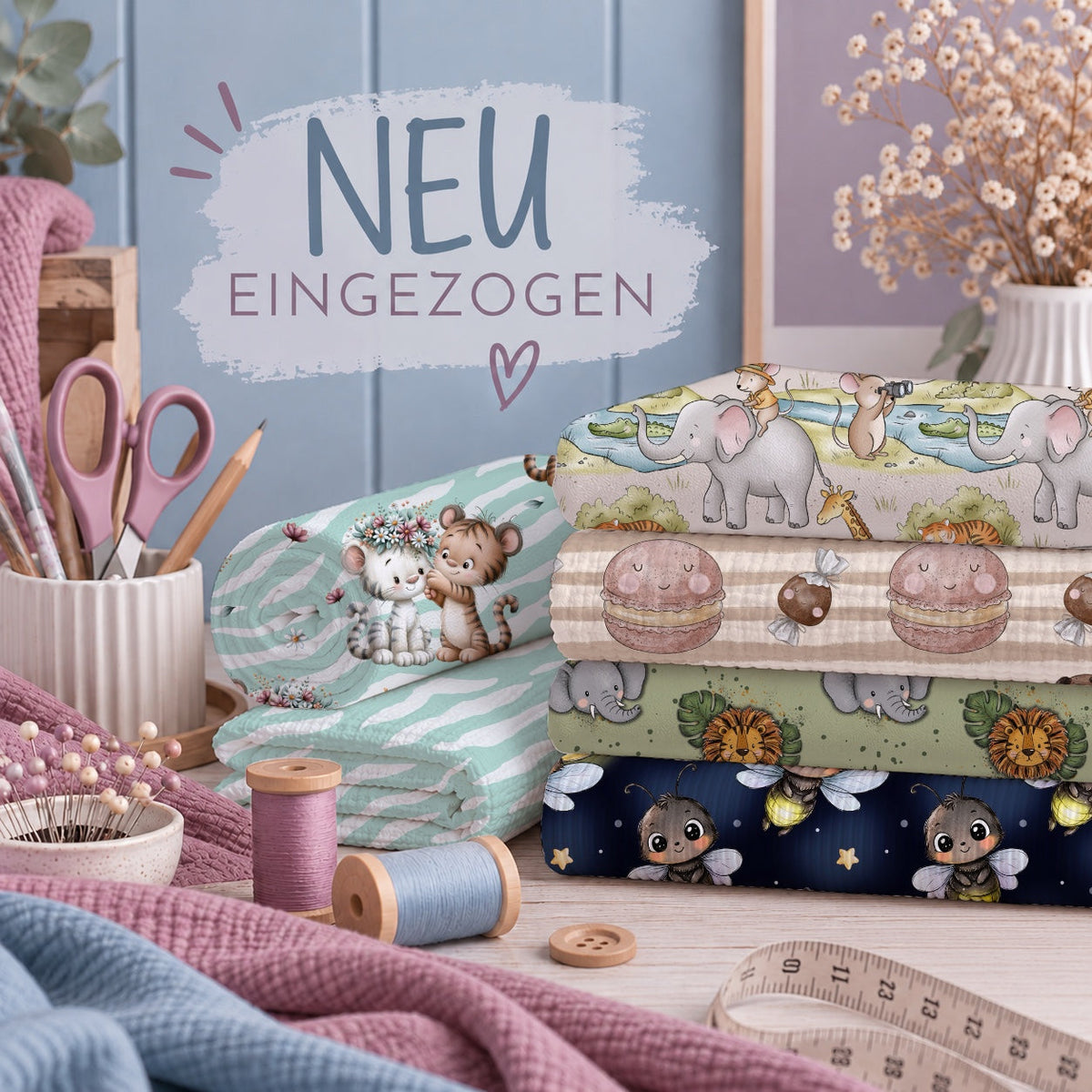 Kollektion Neu Eingezogen: Stapel gemusterter Stoffe mit Elefanten, Macarons, Safaritieren und Bienen. Daneben Minzstoff mit Tigerjungen, Schere, Garn und Maßband. Text: „NEU EINGEZOGEN“.