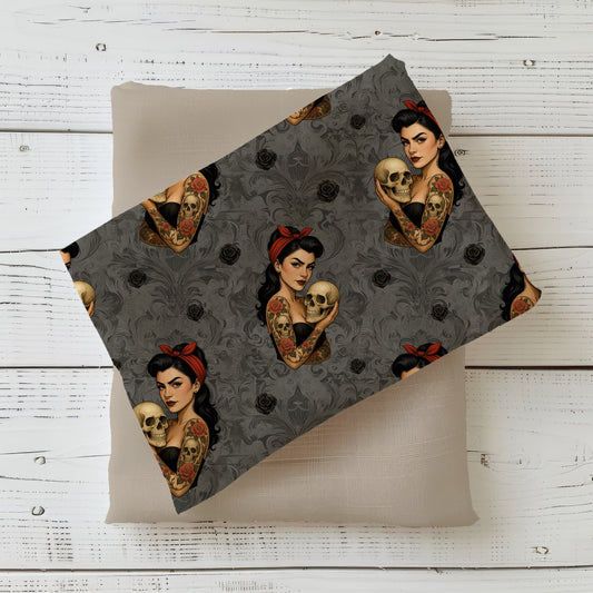 Gefalteter Dark Pinup Stoff – Pin-up Girl mit Tattoos, Totenschädel und roten Akzenten auf dunkelgrauem Ornament-Hintergrund, drapiert auf taupefarbenem Kombistoff
