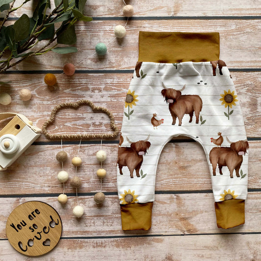 Handgemachte Baby-Pumphose mit Hochlandrind-Motiv, Hühnern und Sonnenblumen – aus Bio-Baumwolle mit Bündchen in dunklem Curry-Gelb.