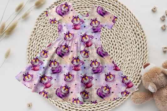 Kinder-Drehkleid mit Grinsekater-Motiv auf buntem Hintergrund – aus weichem Bio-French Terry, perfekt für kleine Entdeckerinnen.