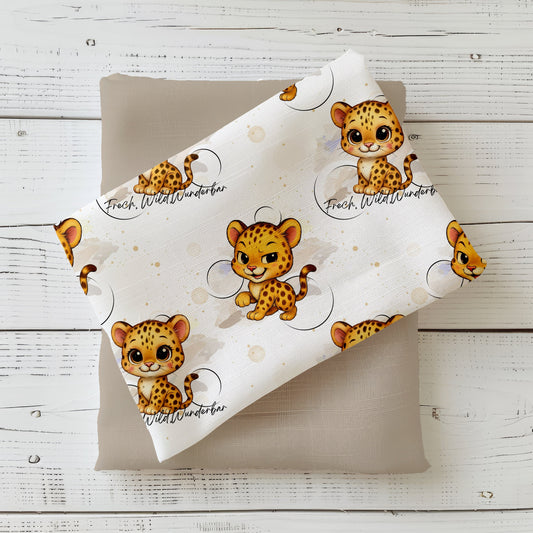 gefalteter Stoff mit dem Design „Frecher Leopard“: bedruckt mit zwei süßen Leoparden‑Babys, einem Aquarell‑Hintergrund in Beige‑Tönen, goldenen Sternchen und dem Spruch „Frech, Wild, Wunderbar“, gerollt und bereit zum Vernähen.