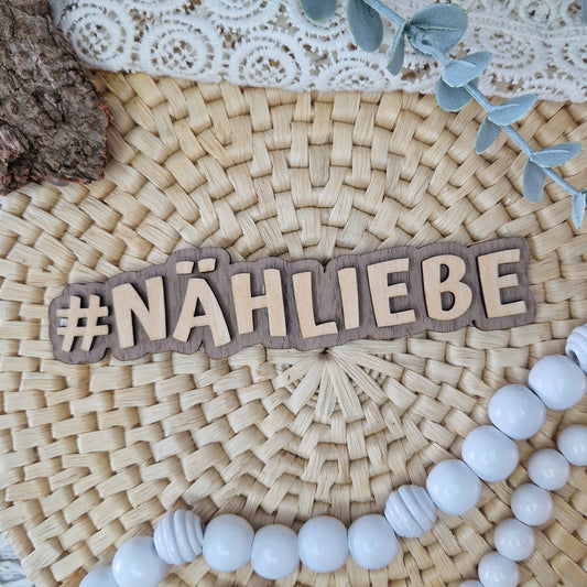 Dekorativer Holzschriftzug #NÄHLIEBE auf geflochtener Unterlage mit DIY-Deko – ideal für Flatlays von Nähprojekten und handgemachten Produkten.