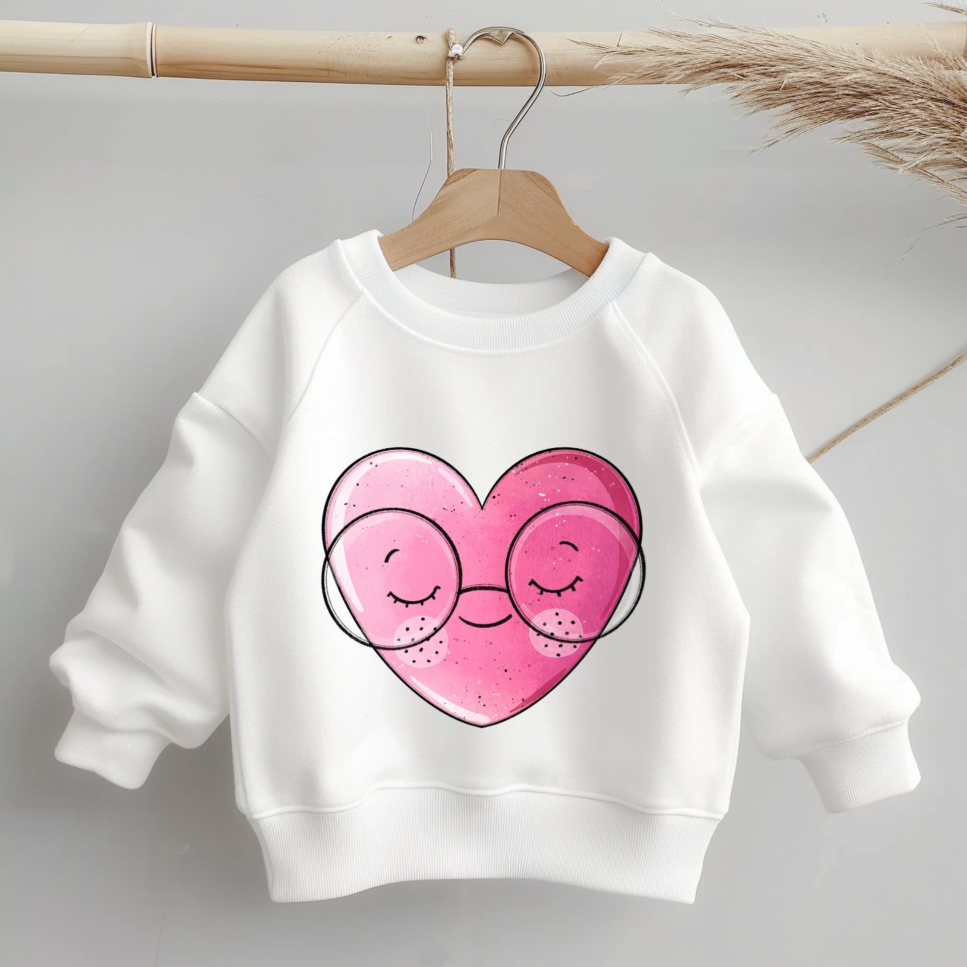 „Mockup eines einfarbigen Kinder-Sweaters: mittig auf der Brust das Bügelbild eines rosa Herzens mit runder Brille; zeigt Größe und Platzierung des Motivs.“