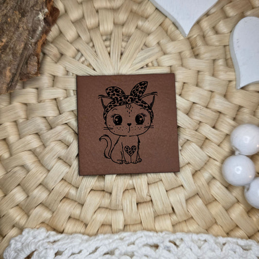 Quadratisches Kunstlederlabel mit gravierter Katze mit Schleife und Leo-Details, Motivdesign von Katzengold-Designs, gefertigt von Stich & Schere