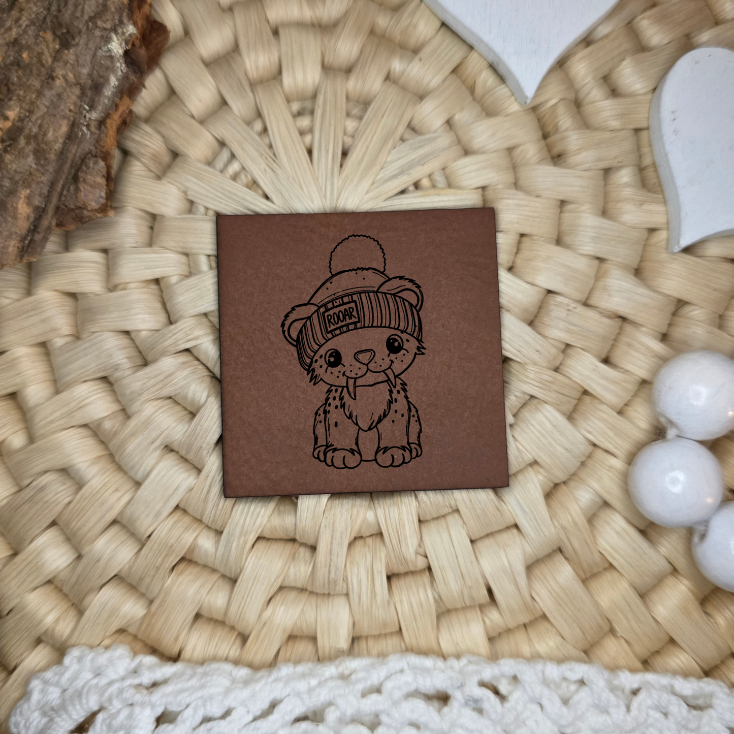 Quadratisches Kunstlederlabel mit graviertem Säbelzahntiger mit Mütze und Schriftzug Roaar, Motivdesign von Katzengold-Designs, gefertigt von Stich & Schere