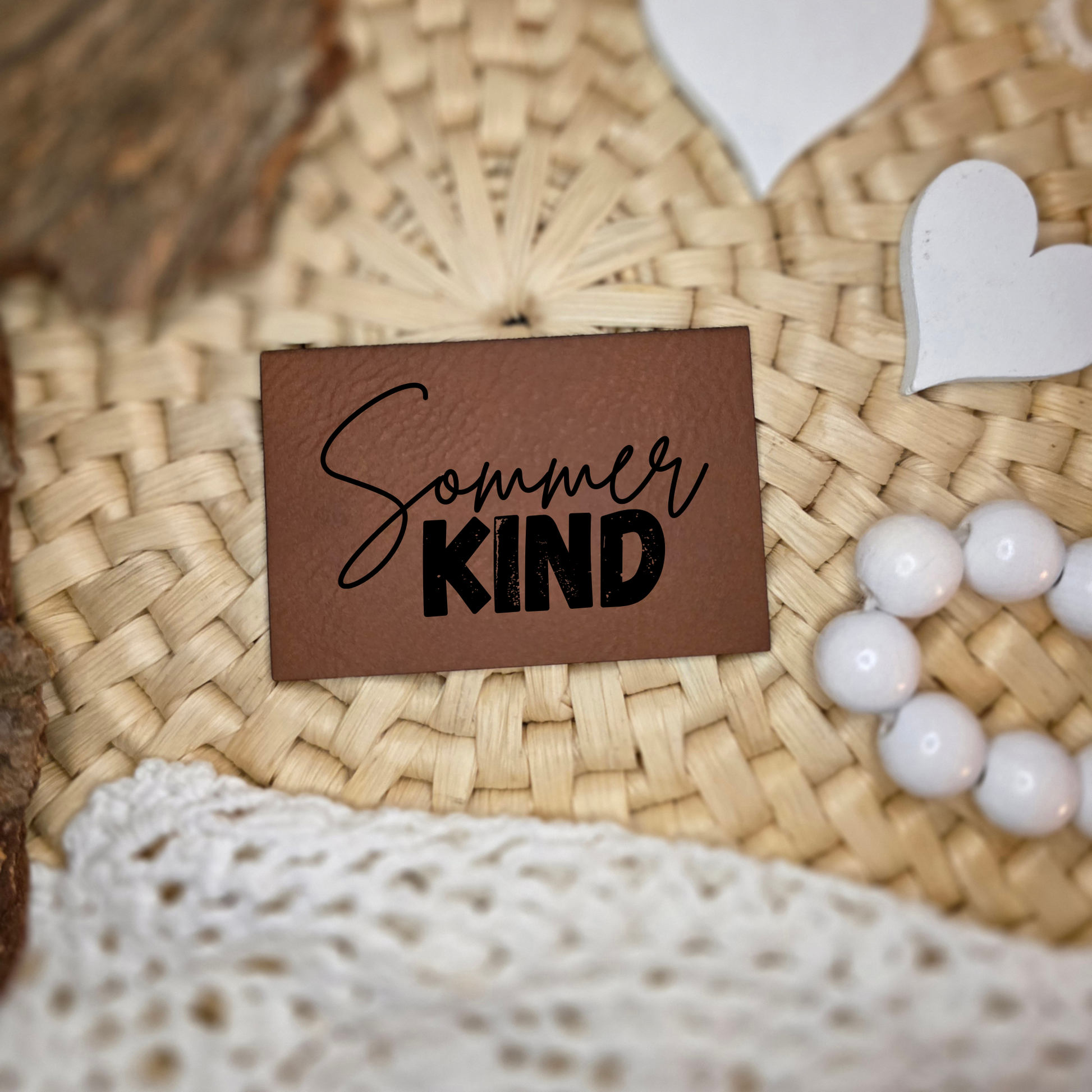 Kunstlederlabel „Sommerkind“ in Braun mit schwarzer Gravur auf geflochtener Unterlage dekorativ platziert