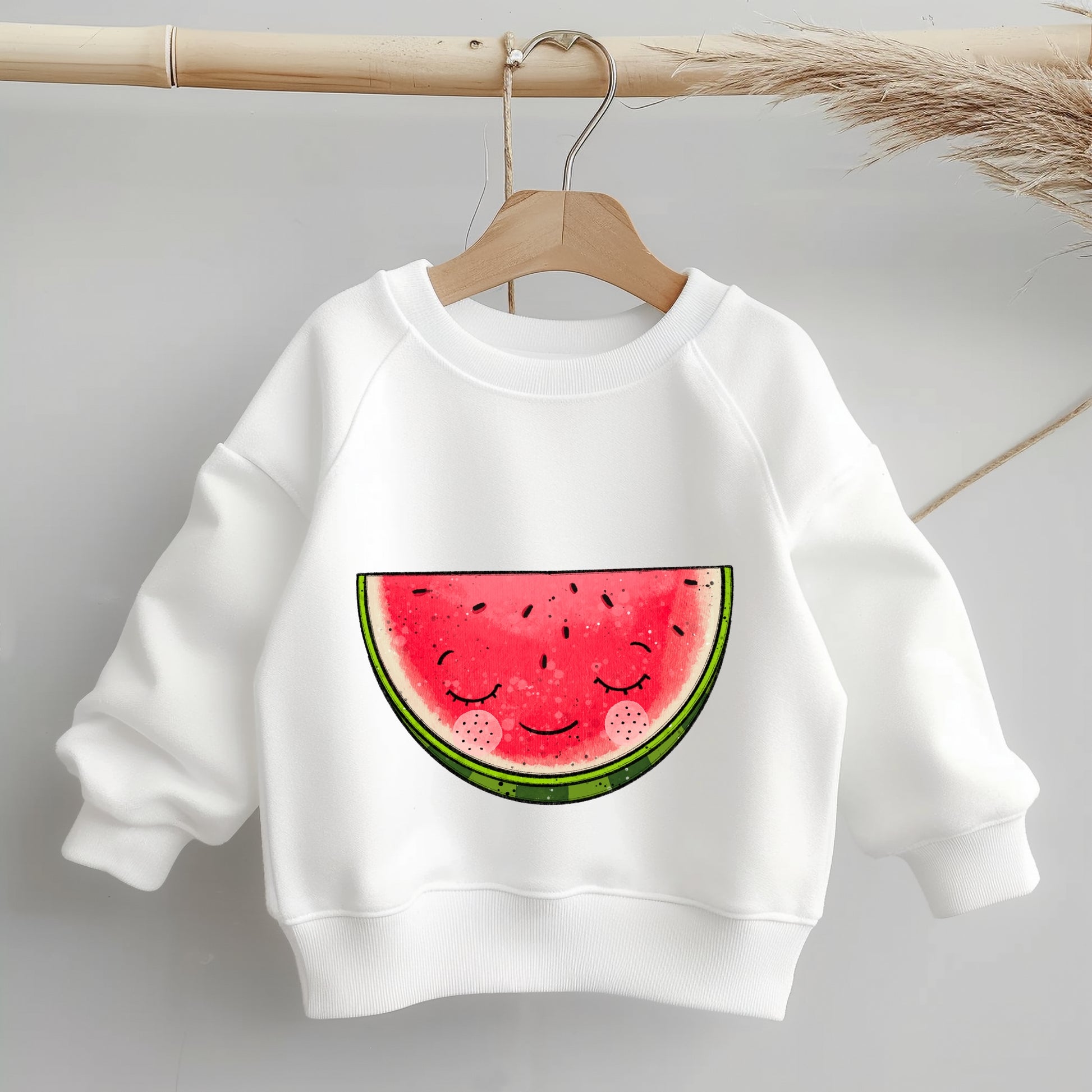 „Mockup eines einfarbigen Kinder-Sweaters: Mittig auf der Brust das Bügelbild einer halben, lächelnden Wassermelone; zeigt Größe und Platzierung des Motivs auf Kleidung.“