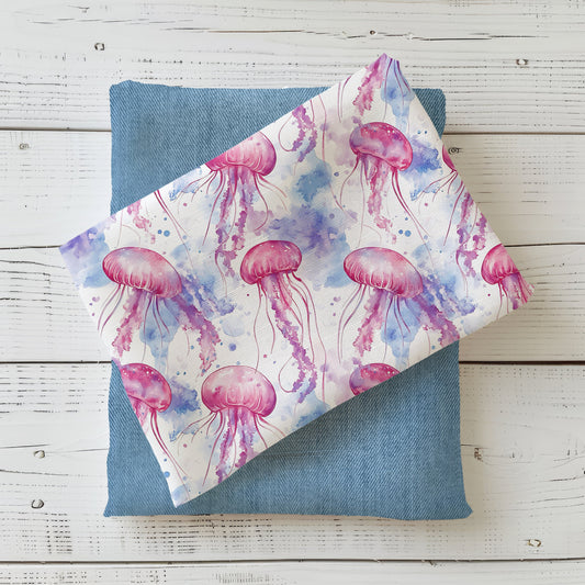 Stoff „Aquarell Quallentanz“ mit pinken und lilafarbenen Quallen sowie blauen Aquarelleffekten, kombiniert mit einem jeansblauen Stoff.