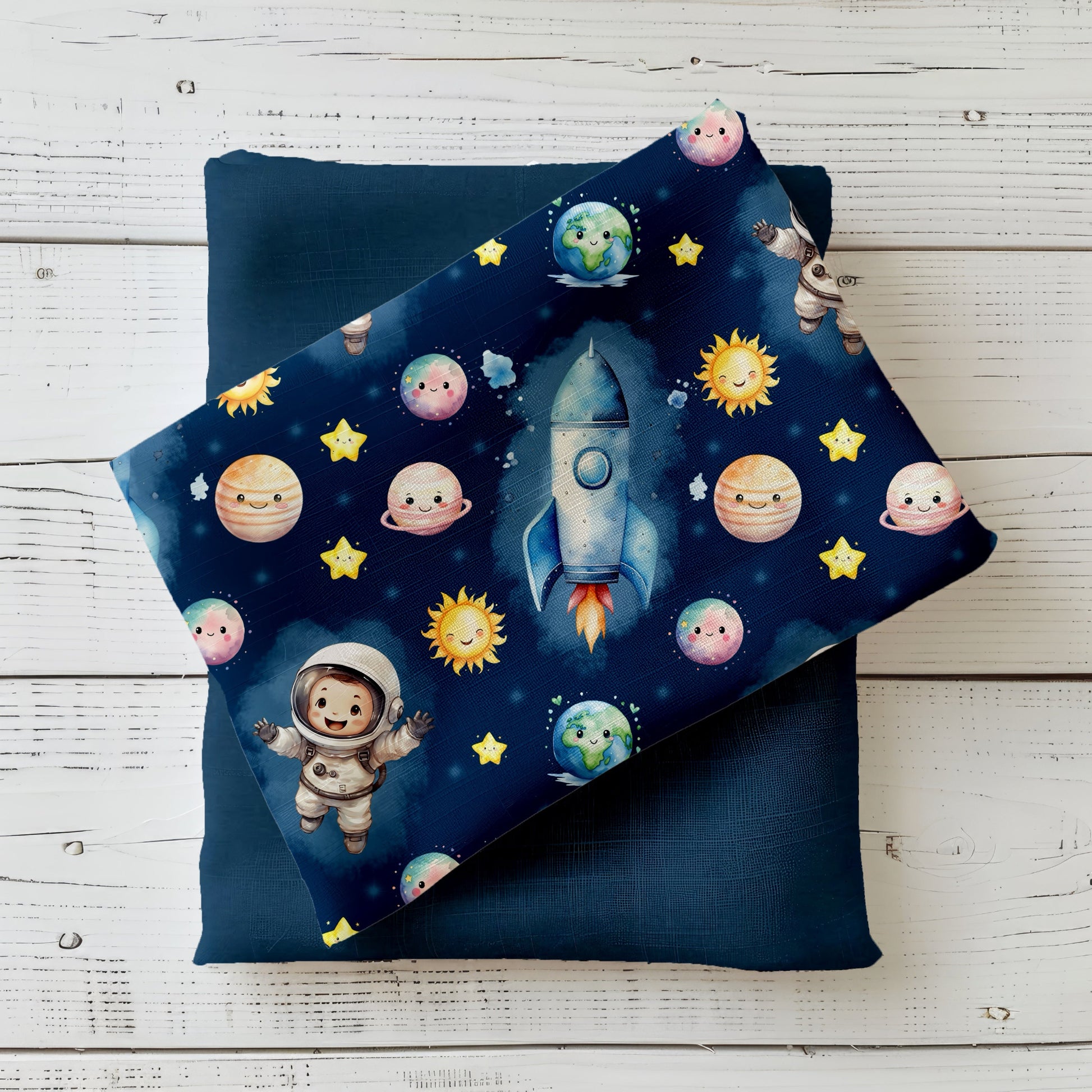 Mockup mit dunkelblauem Astronauten-Stoff: kindlicher Weltraum-Print mit Rakete, Planeten, Sonne, Sternen und kleinem Astronauten – präsentiert auf gefaltetem Uni-Stoff in Dunkelblau, dekoriert auf hellem Holzuntergrund.