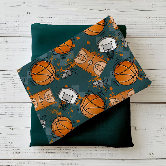 Basketballstoff mit orangefarbenen Basketbällen, Körben und Spielfeldern auf dunklem Petrol im Flatlay