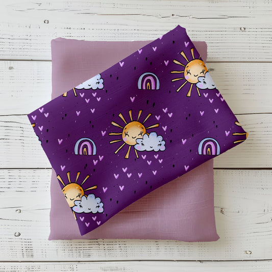 Mockup: Stoff „Believe in Magic Sonne“ – lächelnde Sonne mit Wolke, kleine Herzen & Regenbögen auf violettem Grund; Stoffkachel diagonal auf passendem Uni platziert.