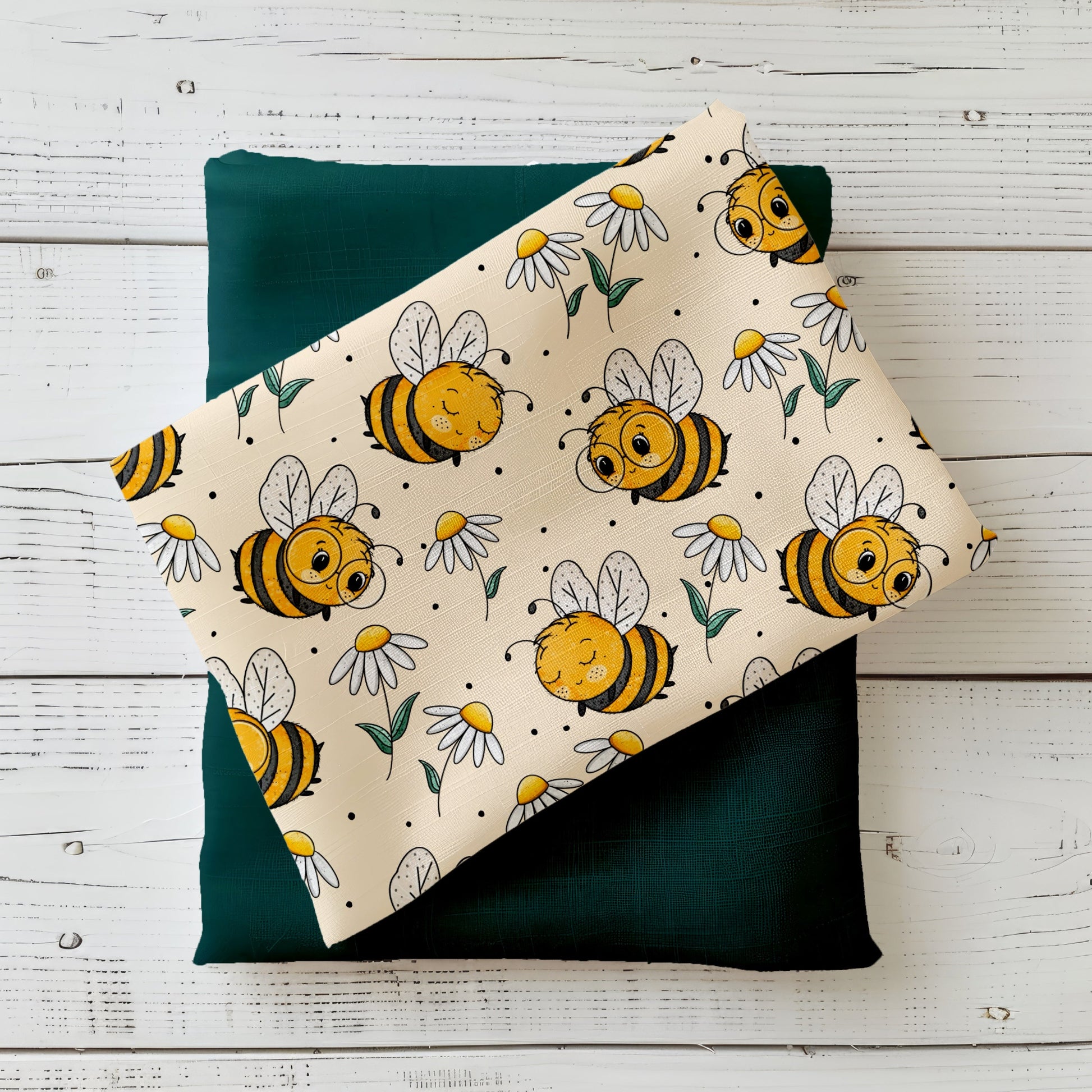 cremefarbener Stoff mit süßen gelben Bienchen und Gänseblümchen, kombiniert mit dunkelgrünem Stoff, aufgenommen auf weißem Holz