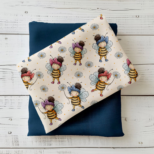 Stoff-Mockup mit dem Design „Bienenmädchen“: hellgrundiger Stoff mit liebevoll illustrierten Bienenmädchen, kleinen Gänseblümchen und feinen Punkten. Der Stoff ist locker gefaltet arrangiert und mit einem dunklen Uni-Kombistoff kombiniert, um Farbwirkung, Motivgröße und Kombinierbarkeit der Meterware zu zeigen. Design von Katzengold-Designs.