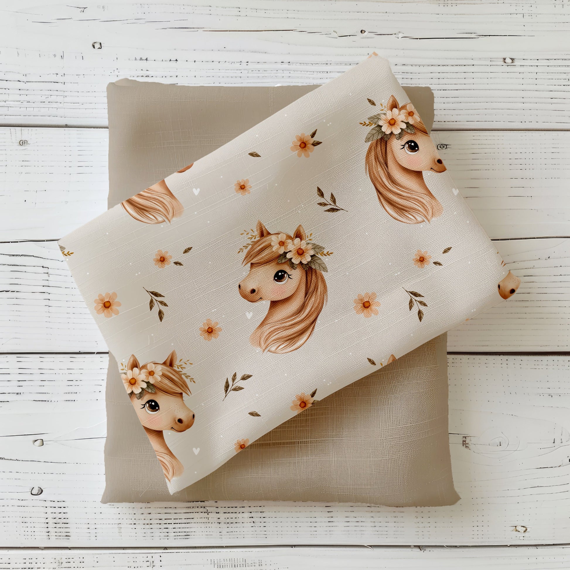 Stoffstück mit hellem Blumenpferd-Design, Pferdeköpfchen mit Blumenkranz und Blüten auf beigem Hintergrund, dekorativ auf Uni-Stoff drapiert.