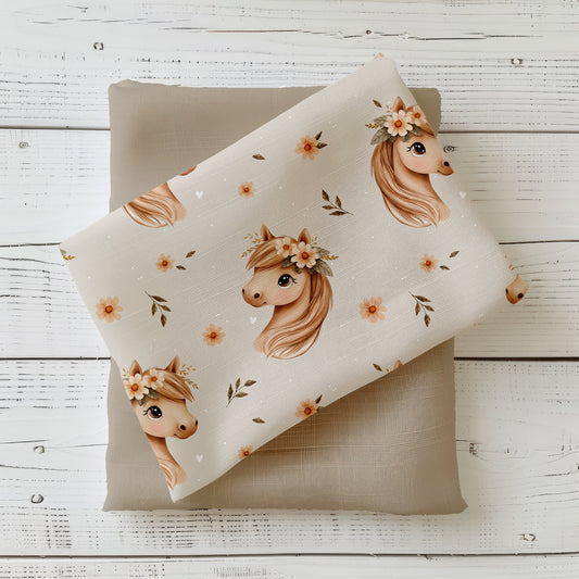 Stoffstück mit hellem Blumenpferd-Design, Pferdeköpfchen mit Blumenkranz und Blüten auf beigem Hintergrund, dekorativ auf Uni-Stoff drapiert.