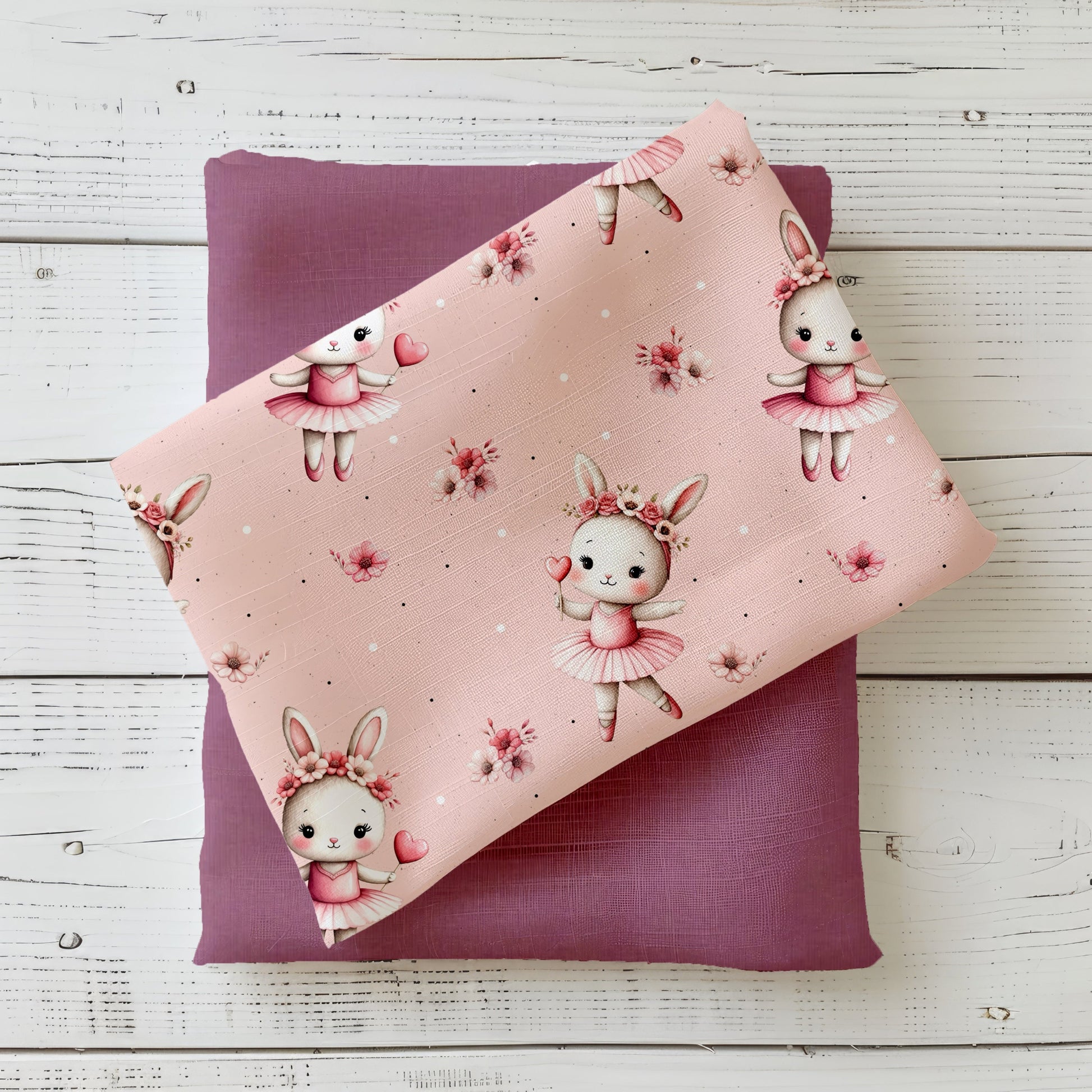 Gefalteter Stoff „Bunny Ballerina“ mit tanzenden Häschen auf roséfarbenem Hintergrund, präsentiert auf passendem Mauve-Unistoff im Flatlay.