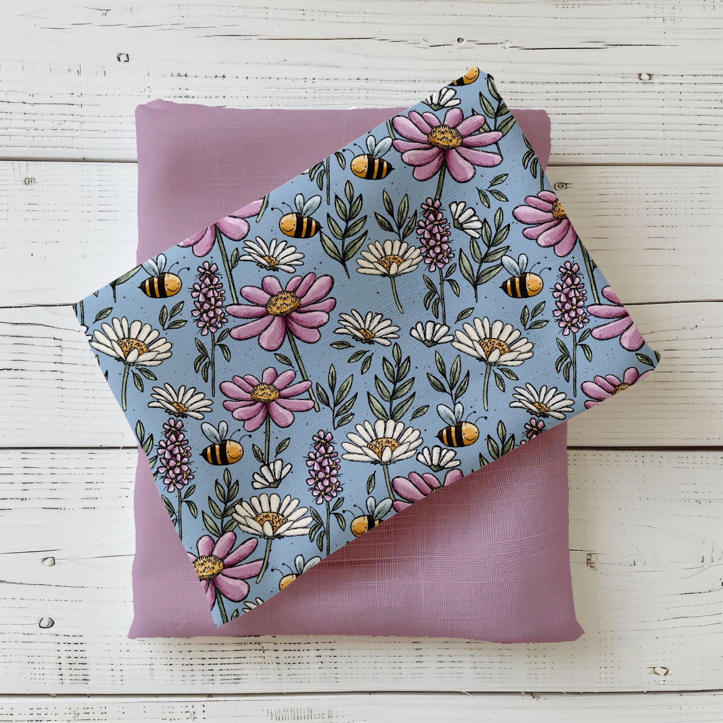 Gefalteter „Bunte Wiese“ Stoff von Katzengold-Designs – farbenfrohe Blumen, Blätter und kleine Bienen auf blaugrünem Hintergrund, dekorativ auf fliederfarbenem Kombistoff präsentiert