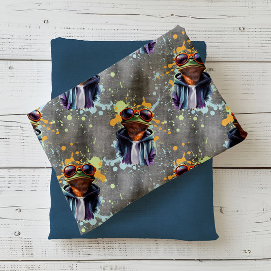 Gefalteter Stoff vom Design „Crazy Frog“ mit buntem Streetstyle-Frosch auf grauem Hintergrund.
