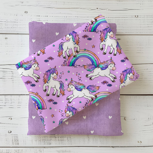 Einhorntraum Einhornstoff mit bunten Einhörnern, Regenbögen, Sternen und Blüten auf lilafarbenem Hintergrund im Flatlay
