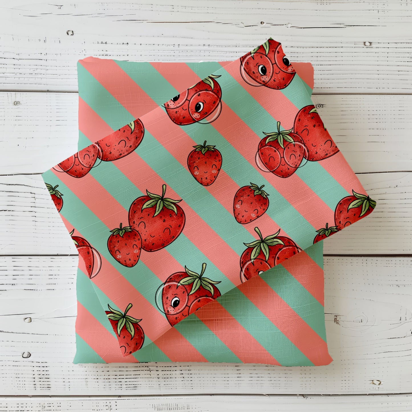 mint- und apricotfarbener Stoff mit süßen Erdbeeren und Gesichtern, kombiniert mit passendem gestreiften Stoff, auf weißem Holz fotografiert
