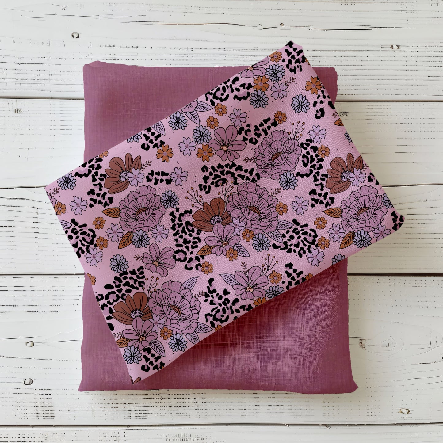 roséfarbener Stoff mit floralen Illustrationen und Leo-Akzenten, kombiniert mit Uni-Mauve Stoff, auf weißem Holz fotografiert