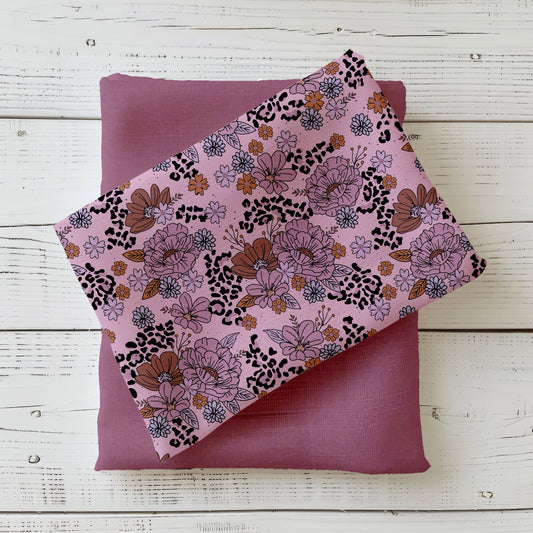 roséfarbener Stoff mit floralen Illustrationen und Leo-Akzenten, kombiniert mit Uni-Mauve Stoff, auf weißem Holz fotografiert