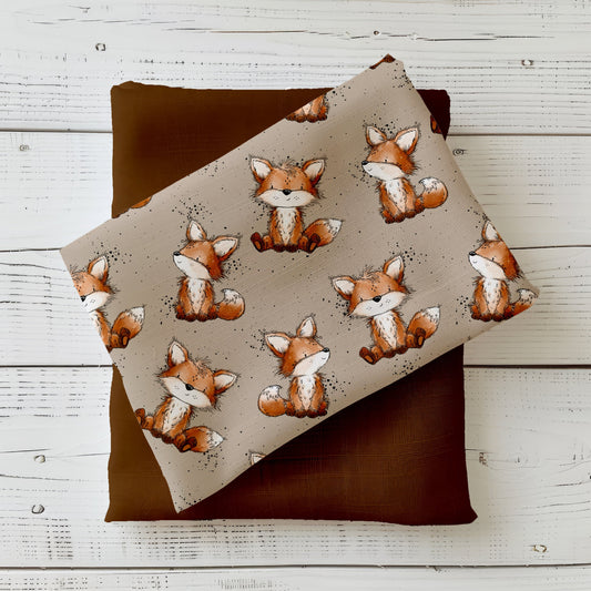 Stoff-Mockup „Fuchstag“ mit niedlichen, handgezeichneten Füchsen auf ruhigem, naturfarbenem Hintergrund, kombiniert mit warmem Uni-Stoff in Braun- und Rosttönen.