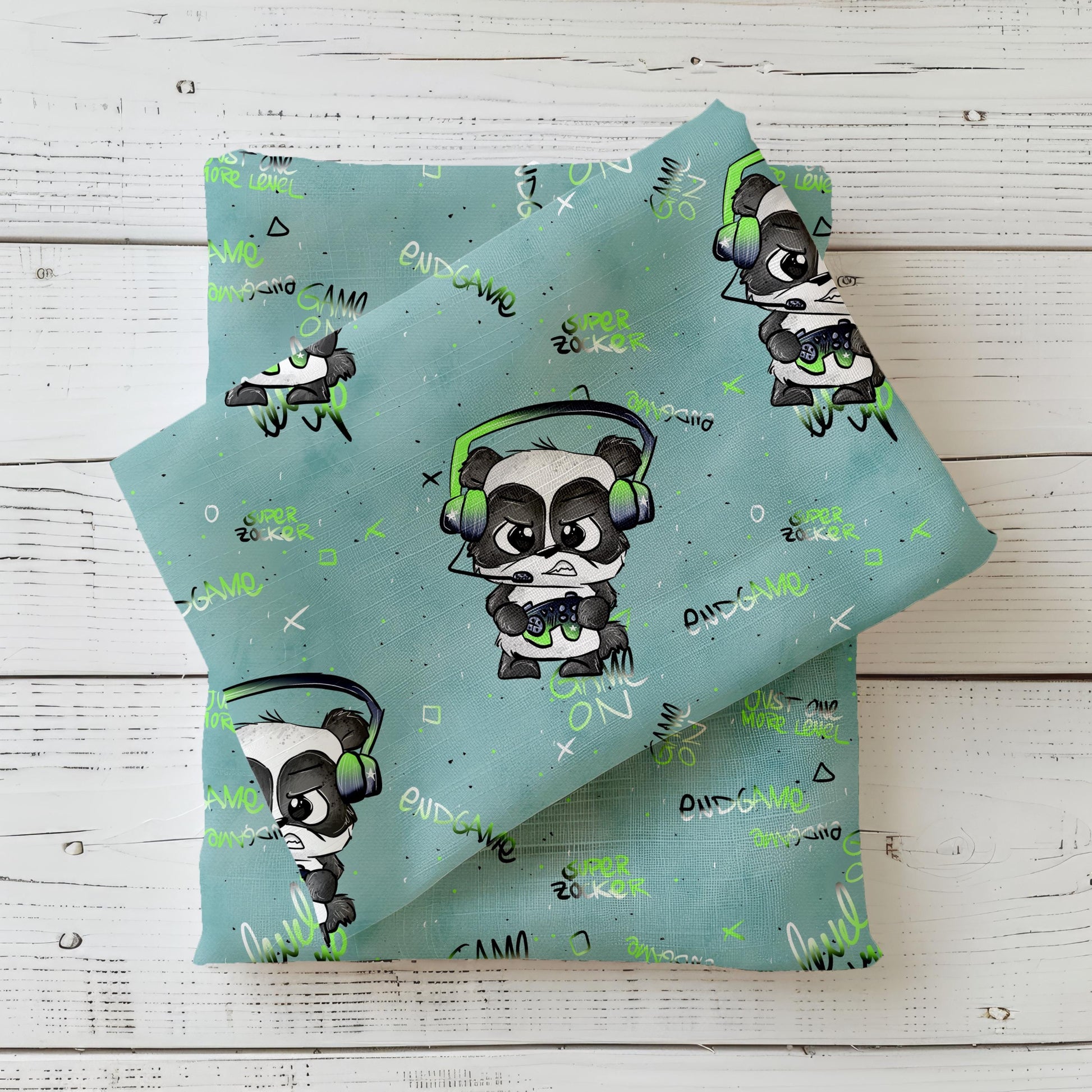 Gefalteter Kinderstoff Gamepanda von Schnubbirella im Mockup – mintfarbener Hintergrund mit Panda-Gamer-Motiv, Headset, Controller und Gamer-Schriftzügen, drapiert auf dunkelgrünem Kombistoff.