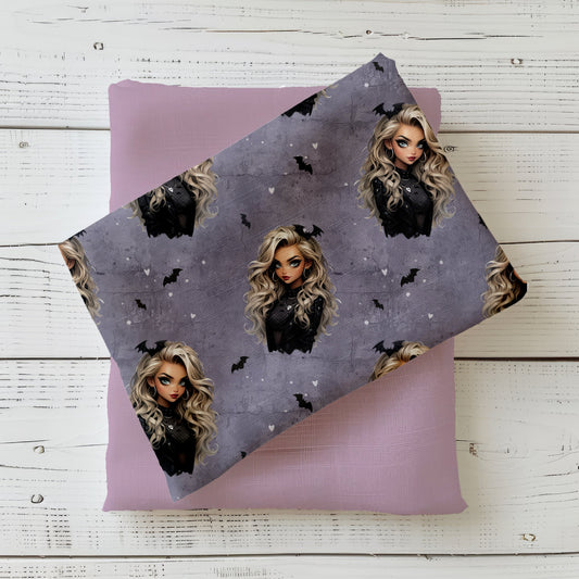Gefalteter Stoff mit dem Design  "Gothic Glam" in lila – eine Frau mit lockigen blonden Haaren mit Fledermaus im Haar, schwarz gekleidet auf einem lilafarbenen Hintergrund in Beton Optik mit Rissen. Kleine schwarze Fledermäuse und weiße herzen befinden sich in den Zwischenräumen.