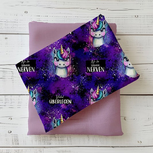 Stoff-Mockup „Grumpycorn – Lila“ mit frechem Einhorn und Regenbogenmähne, dekorativ über einem passenden Uni-Stoff fotografiert.