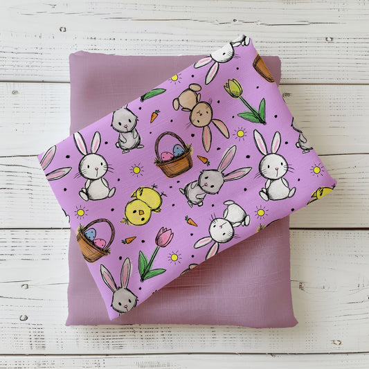 Hasenglück Lavendel Stoffdesign mit Hasen, Küken, Ostereiern, Karotten und Tulpen auf lavendelfarbenem Hintergrund