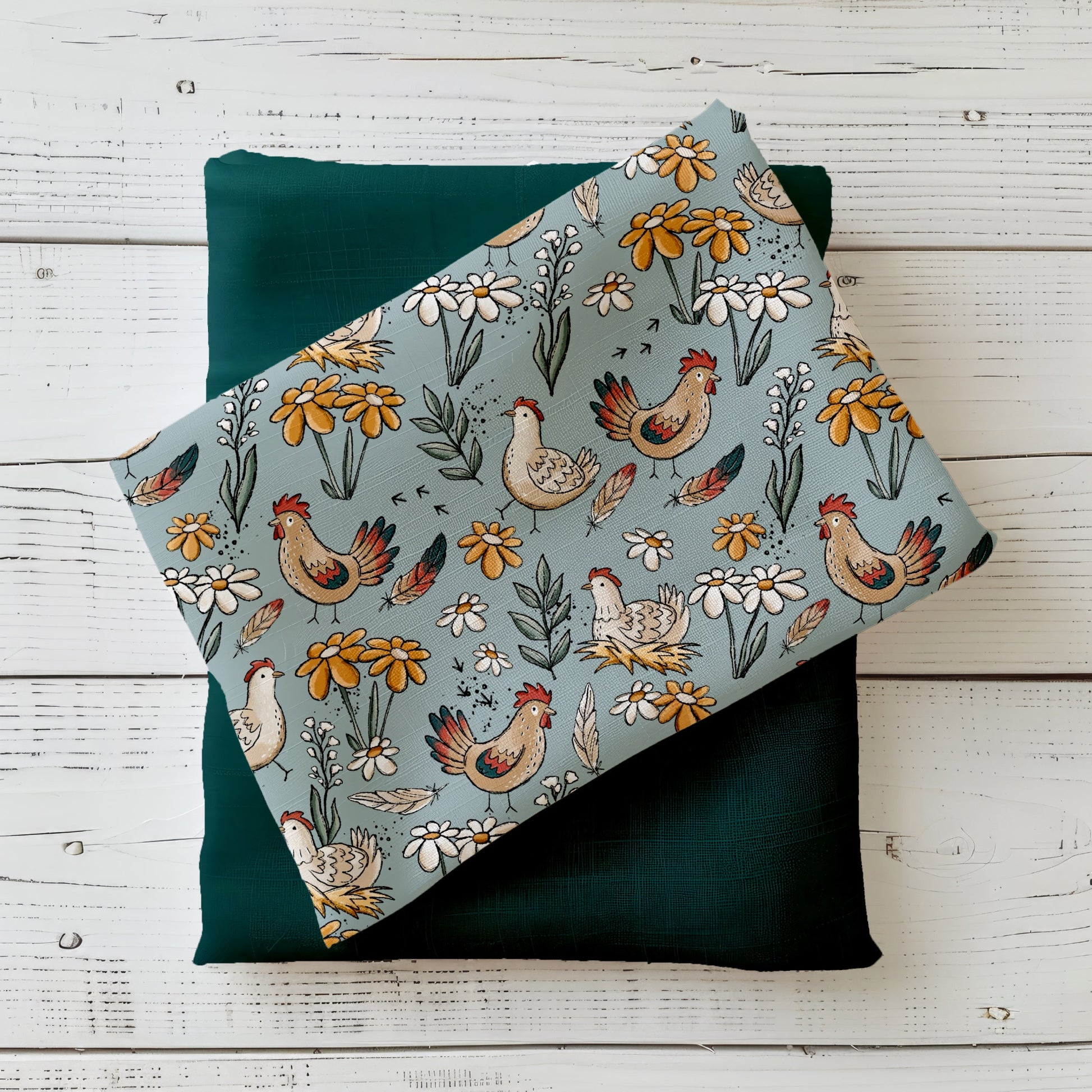 Gefalteter Hühnertag Stoff von Katzengold-Designs – verspielte Hühner, Blumen und Federn auf blaugrünem Hintergrund, drapiert auf dunkelgrünem Kombistoff