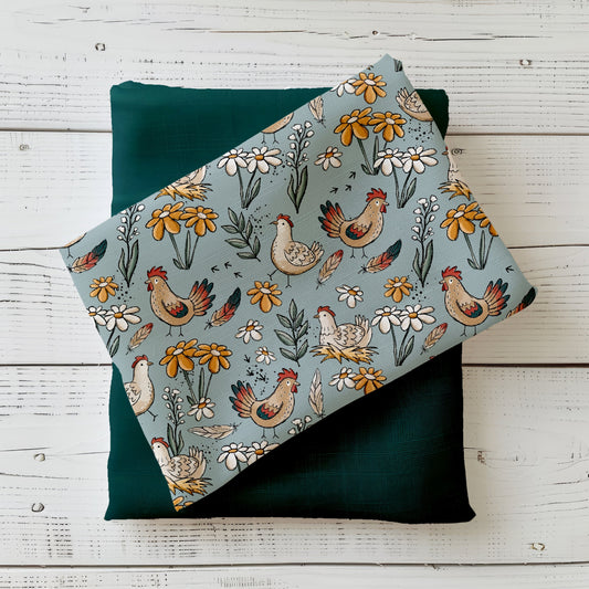 Gefalteter Hühnertag Stoff von Katzengold-Designs – verspielte Hühner, Blumen und Federn auf blaugrünem Hintergrund, drapiert auf dunkelgrünem Kombistoff