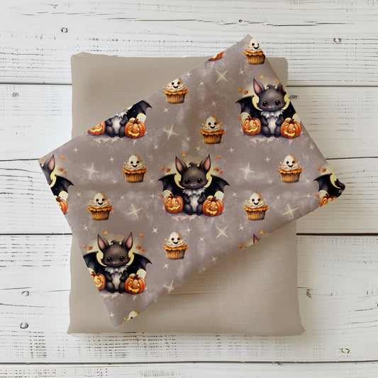 Halloweenstoff „Kleine Fledermaus“ mit süßer Fledermaus, Kürbissen und Cupcakes auf grauem Hintergrund.