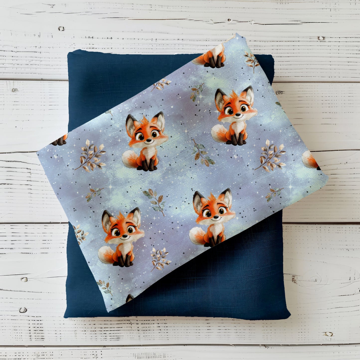 Gefalteter Kinderstoff „Kleiner Fuchs“ im Mockup – süße, illustrierte Füchse auf verträumtem blau-lila Hintergrund, drapiert auf dunklem Uni-Stoff.
