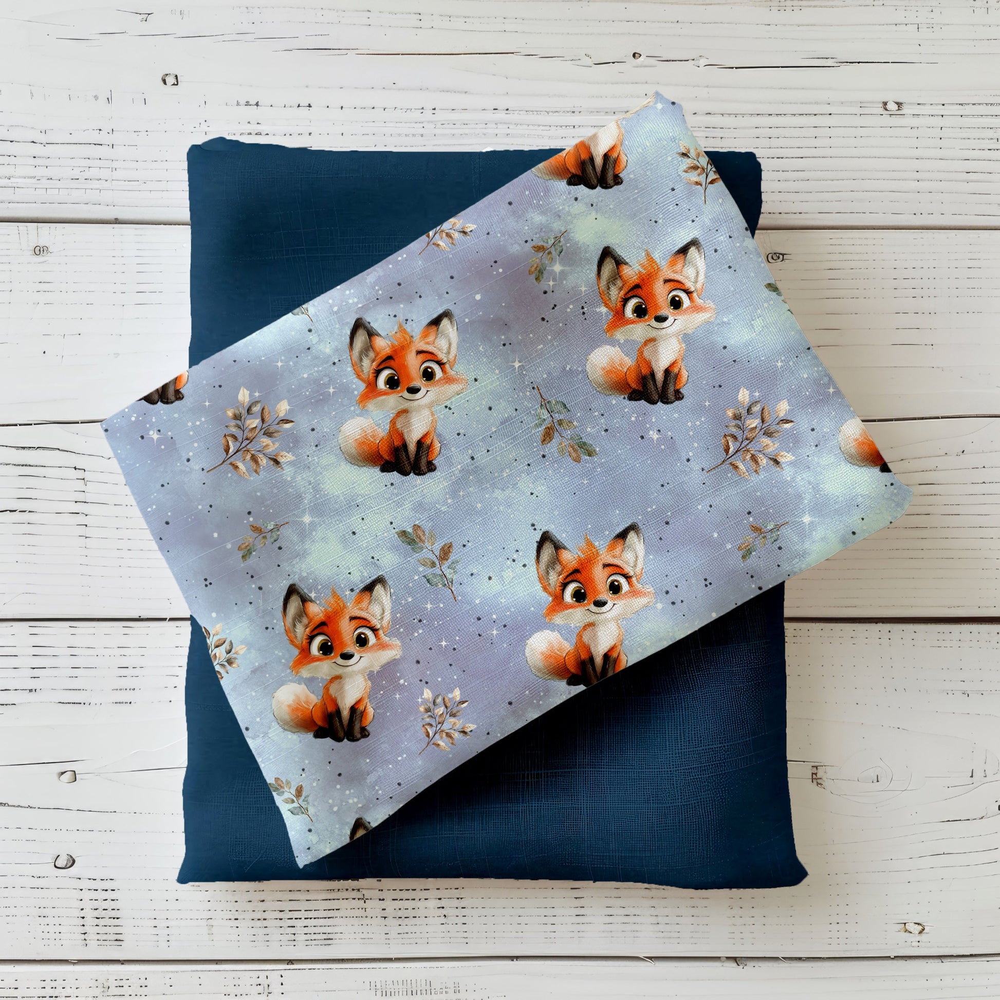 Gefalteter Kinderstoff „Kleiner Fuchs“ im Mockup – süße, illustrierte Füchse auf verträumtem blau-lila Hintergrund, drapiert auf dunklem Uni-Stoff.