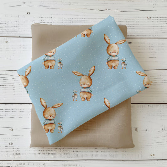 Stoff-Mockup „Hase & Ente“: Gefalteter Kinderstoff in Himmelblau mit kleinen Hasen und Enten, dekorativ auf einem beigen Kombistoff präsentiert.