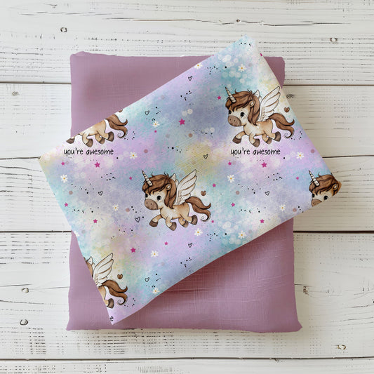 Gefalteter Kinderstoff „Kleines Pony“ in Pastellrosa mit fliegenden Ponys auf einem Stoffstapel in Rosé, dekorativ auf weißem Holz fotografiert.