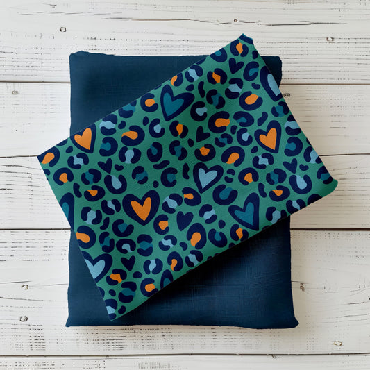 Gefalteter Stoff „Leo Herzen petrol“ mit Leo-Print und Herzmotiven in Petrol, Blau und Ocker auf Holzuntergrund