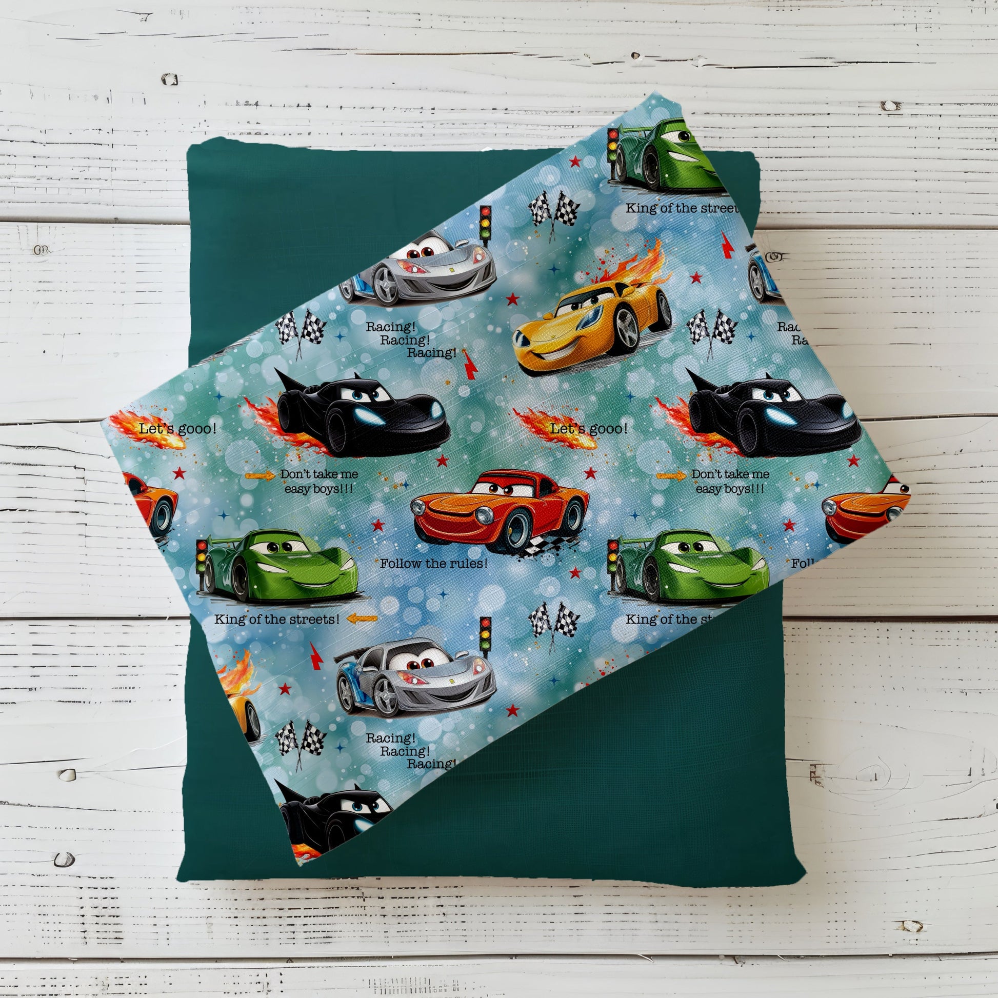 Stoff-Mockup „Let’s Go!!“ mit bunt gemischten Rennwagen und Racing-Details auf hellblauem Hintergrund, drapiert über einem dunklen Unistoff.