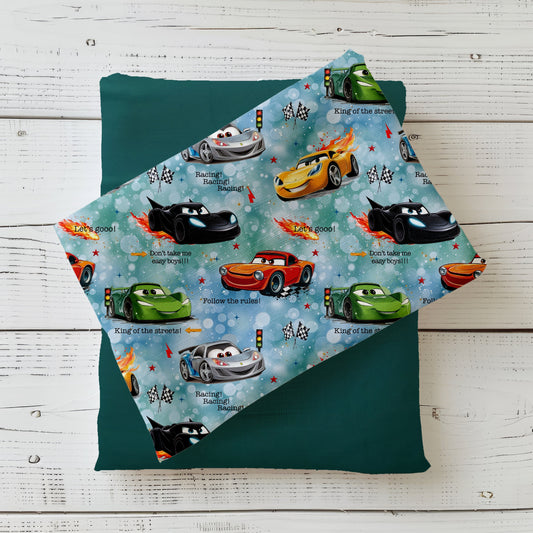 Stoff-Mockup „Let’s Go!!“ mit bunt gemischten Rennwagen und Racing-Details auf hellblauem Hintergrund, drapiert über einem dunklen Unistoff.