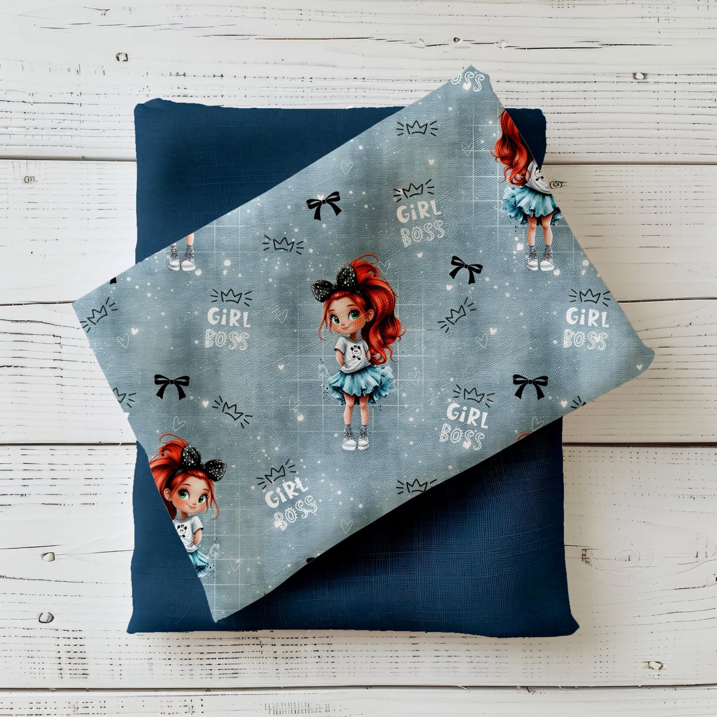 Gefalteter Mini Boss Girl Stoff – Mädchenmotiv mit rotem Haar, funkelnder Schleife und „Girl Boss“ Schriftzügen auf blau-grauem Hintergrund, drapiert auf dunkelblauem Kombistoff
