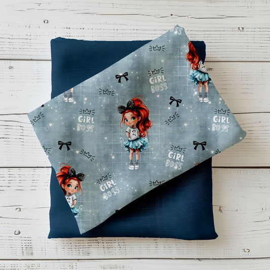 Gefalteter Mini Boss Girl Stoff – Mädchenmotiv mit rotem Haar, funkelnder Schleife und „Girl Boss“ Schriftzügen auf blau-grauem Hintergrund, drapiert auf dunkelblauem Kombistoff
